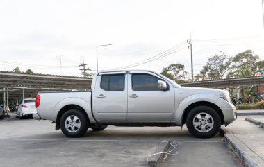Sağ tarafı manzaralı gümüş kamyonet, alışveriş merkezinin açık otoparkına park ediyor..