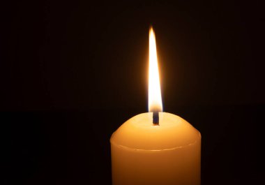 Büyük beyaz bir mumun üzerinde parlayan tek bir mum ya da ışık kilisedeki siyah ya da koyu arkaplanda Noel, cenaze ya da anma töreni için izole edilir.