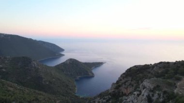 Dağların üzerinden uçmak. Havadan deniz manzaralı yeşil kayalar. Gün batımında mavi deniz lagünbatımında insanlar olmadan çevrili. Yüksek kalite 4k görüntü