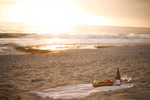 Romantic picnic by the sea at sunset Deserted beach in the warm rays of sunset Champagne and fruit basket. High quality photo