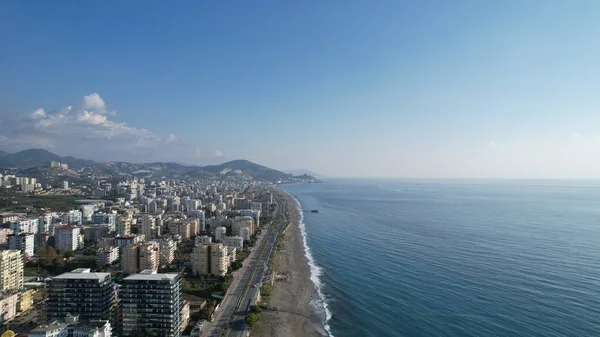 Sahil şeridi boyunca uzanan, manzaralı bir sahil kasabasının havası, uzaktan yükselen görkemli dağların zeminiyle. Yüksek kalite fotoğraf
