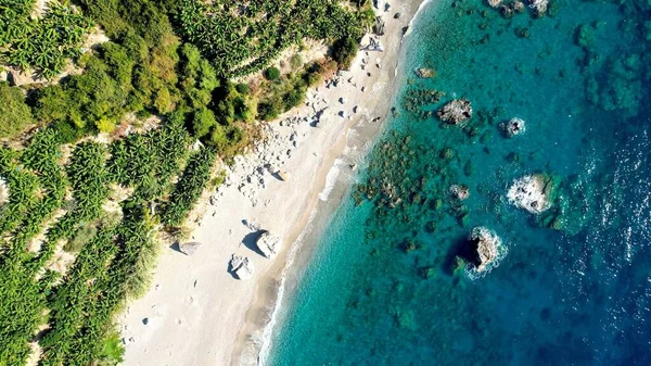 Bereketli bir muz koruluğuna kurulmuş tenha bir plajın yer aldığı havadan çekilmiş bir fotoğraf. Kristal berrak turkuaz suları el değmemiş kumlu sahili kucaklıyor. Huzur ve doğal güzellik vahası yaratıyor.