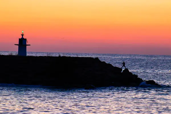 Gün Batımında Kayalık Bir Sahilde Balık Tutan Bir Adamın Silüeti — Stok fotoğraf