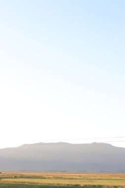 Geniş tarlaları, kırsal alanı ve uzak dağları olan sakin kırsal bir arazide ılık bir gün batımı..