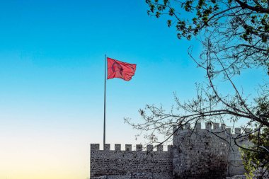 Türk bayrağı, ulusal gururu simgeleyen antik taş bir kalenin üzerindeki açık mavi gökyüzüne gururla dalgalanıyor. Erzurum kalesi, Türkiye.
