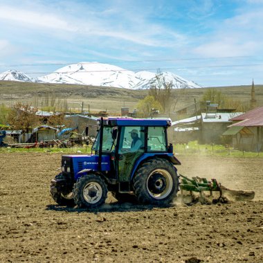 Çiftçilik: güçlü bir traktör toprağı sürükler, toprağı uzak tepelerdeki uzun süren kar örtüsüne karşı yeni bir büyüme döngüsü için hazırlar. Yüksek kalite fotoğraf