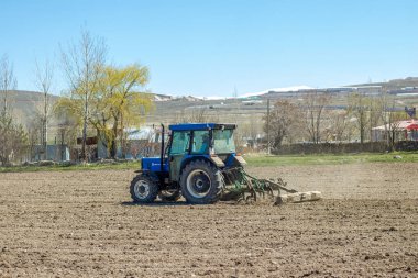 Farming: a powerful tractor tills the earth, readying the soil for a new cycle of growth against a backdrop of lingering snow on distant hills. High quality photo clipart