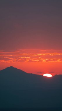 Bir dağın arkasında sakin bir günbatımı, gökyüzünde sıcak bir parıltı, geniş metin alanı olan arka planlar için mükemmel. Görüntü bir yolculuğun sonunu ve yeni bir başlangıcın vaadini simgeler..