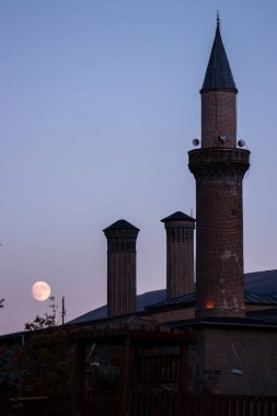 Arkasında dolunay olan Erzurum Ulu Camii ve Double Minaret Madrasa 'yı gösteren çarpıcı bir görüntü. Bu fotoğraf, bu tarihi mekanın mimari güzelliğini yansıtıyor.