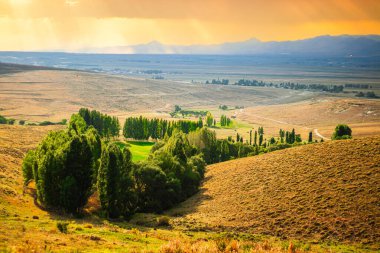 Cayirtepe, Erzurum, Türkiye 'de geniş bir bozkırla çevrili canlı yeşil bir vadinin manzarası. Resim metin için geniş bir alan sunuyor, sükuneti ve dokunulmamış doğanın güzelliğini sembolize ediyor.