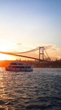 İstanbul 'un güzelliğini ve sükunetini yansıtan ikonik köprüsü ve feribotuyla Boğaz' ın üzerinde sakin bir günbatımı. Dikey duvar kağıdı arkaplanı için mükemmel.
