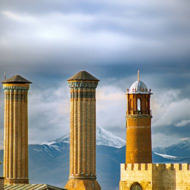 Erzurum Twin Minaret Madrasa and Clock Tower, iconic landmarks framed by snowy mountains and dramatic skies, representing the city's rich history and cultural pride.  clipart