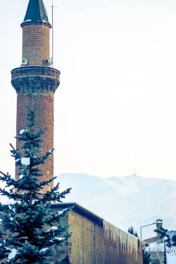 The historic minaret of Erzurum Ulu Mosque stands tall with the snow-covered Palandoken Mountain in the background, showcasing cultural heritage and natural beauty in harmony. clipart