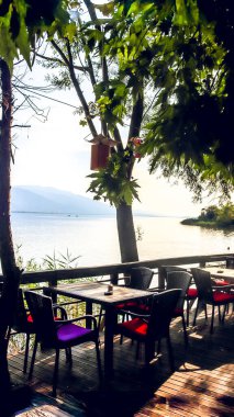 Sapanca Gölü 'nde sakin bir göl kafesi. Ahşap masalar, renkli sandalyeler ve yemyeşil yapraklar sakin sularda geçmişe dönük bir kaçış sağlıyor..