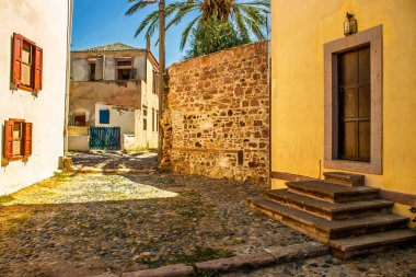 Edremit, Balikesir 'de yazın dingin cazibesini yansıtan, kırsal mimari, palmiye ağaçları ve altın güneş ışığıyla süslenmiş sakin bir kaldırım taşı caddesi. Seyahat kavramları için mükemmel.