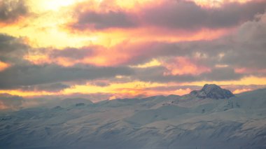 A peaceful winter landscape with distant mountains under a calm dramatic sky at sunset. clipart