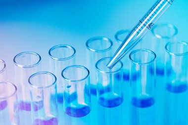 Test tubes with blue liquid water samples and pipette over blue background. Laboratory glassware, science laboratory research concept.