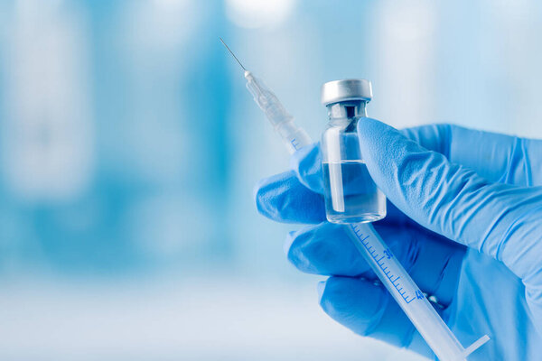 Doctor's hand holding glass vial and syringe with injection over blue background. Vaccination or beauty therapy concept.