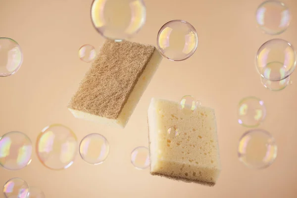 Natural dishwashing sponge with soap bubbles over beige background. Eco friendly housework objects.