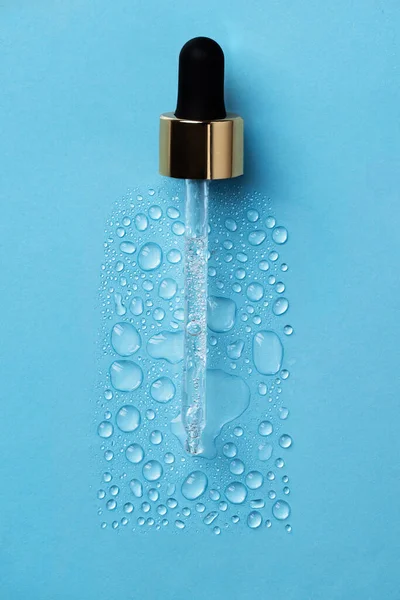 Drops of face serum top view. Liquid gel moisturizer. Creative idea of face serum with pipette on blue background.