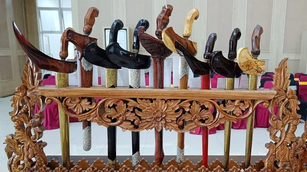Various keris or traditional Indonesian weapons with unique wood carvings are arranged in place of weapons
