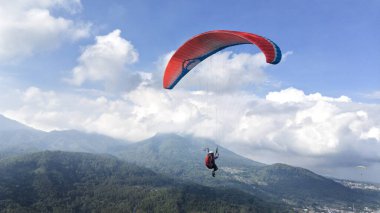 Mavi gökyüzünde ve dağ manzarasında uçan paraglider