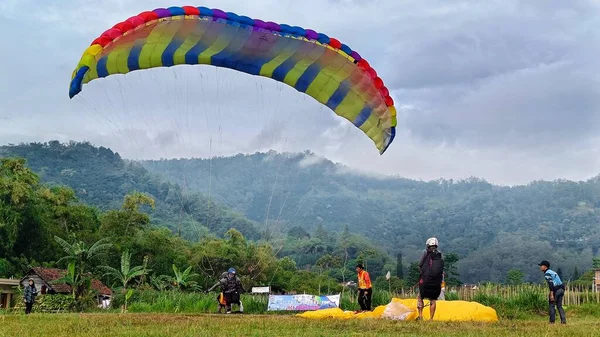 2023年7月8日インドネシア東ジャワ州バトゥ市の飛行場にカラフルなパラシュート着陸のパラグライダーパイロット — ストック写真