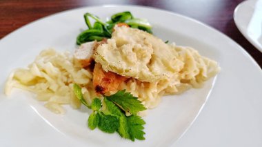 Izgara tavuk dilimleri, lezzetli çıtır makarna ve beyaz tabakta servis edilen sebzeler.