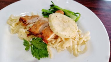 Izgara tavuk dilimleri, lezzetli çıtır makarna ve beyaz tabakta servis edilen sebzeler.