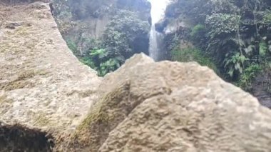 Yeşil bir ormanın ortasında büyük doğal kayaların olduğu şelale manzarası.