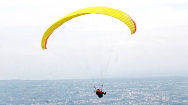 Paraşütçü pilot mavi gökyüzünde beyaz bulutlarla uçuyor.