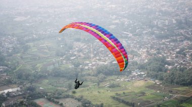 Paraglider köy manzarası ve mavi gökyüzü arkaplanı üzerinde uçuyor
