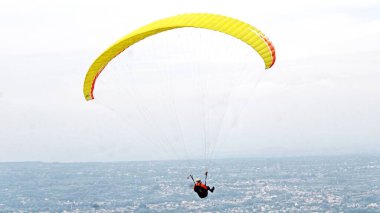 Paraşütçü pilot mavi gökyüzünde beyaz bulutlarla uçuyor.