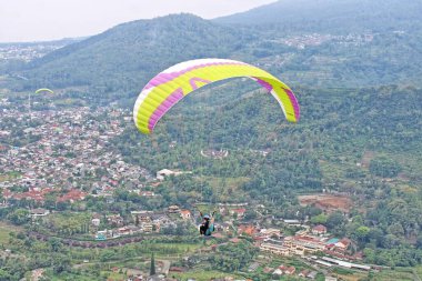 Paraglider pilotu mavi gökyüzünde uçuyor köy ve dağ manzaralı