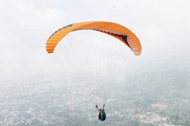 Paraşütçü pilot mavi gökyüzünde beyaz bulutlarla uçuyor.