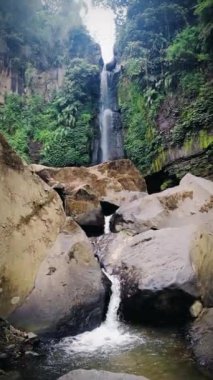 Yeşil ormanın ortasında büyük doğal kayaların olduğu şelale manzarası.
