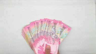 100.000 rupia değerinde bir yığın Endonezya banknotunu tutan el.