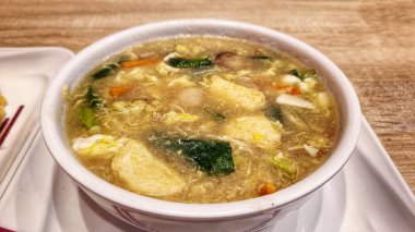 Çorba kalın çorba ve köfte parçaları, deniz ürünleri ve yeşil sebzeler beyaz kasede servis edilir.