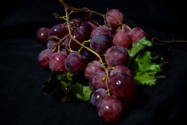 Siyah arka planda yaprakların üzerinde duran üzümler.