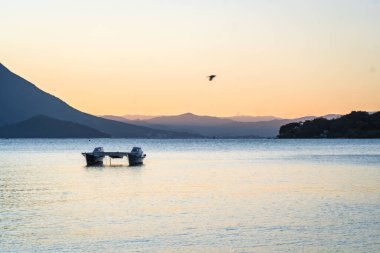 Boş katamaran sakin sularda durdu, güneşli bir günde, arka planda dağlar ve barışçıl bir atmosferle.