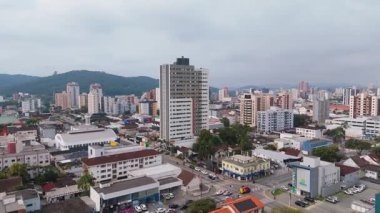 Konut evleri, ticari binalar ve uzak tepelerle dolu canlı bir şehir caddesinin insansız hava aracı görüntüsü