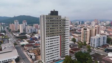 Konut evleri, ticari binalar ve uzak tepelerle dolu canlı bir şehir caddesinin insansız hava aracı görüntüsü