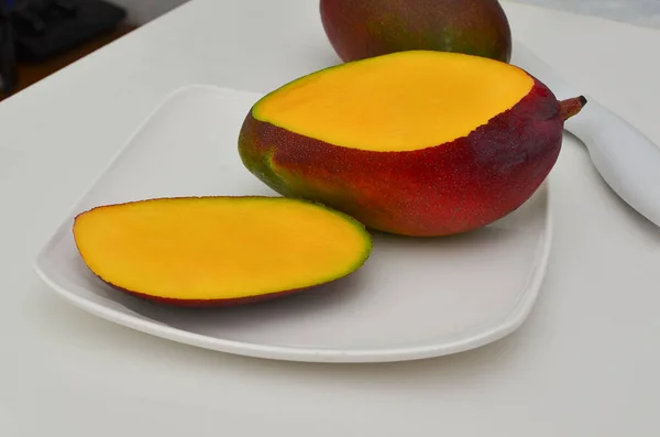 Lezzetli olgun sarı mango dilimleri iştah açıcı bir şekilde beyaz bir tabakta, tropikal renk ve lezzet patlaması.