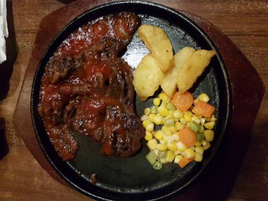 Lezzetli ızgara biftek ve sebze salatalı patates dilimleri tabakta servis ediliyor.