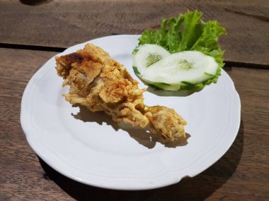 Crispy fried chicken with lettuce and cucumber on white plate