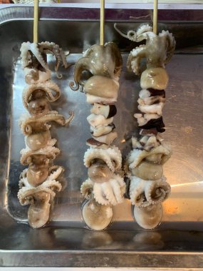 Açık hava yiyecek pazarında servis edilen bambu çubuğuyla ızgara yapılmış lezzetli kalamar ve ahtapot. egzotik Asya yemekleri. 