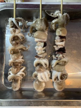 Açık hava yiyecek pazarında servis edilen bambu çubuğuyla ızgara yapılmış lezzetli kalamar ve ahtapot. egzotik Asya yemekleri. 