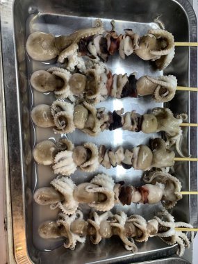 Açık hava yiyecek pazarında servis edilen bambu çubuğuyla ızgara yapılmış lezzetli kalamar ve ahtapot. egzotik Asya yemekleri. 