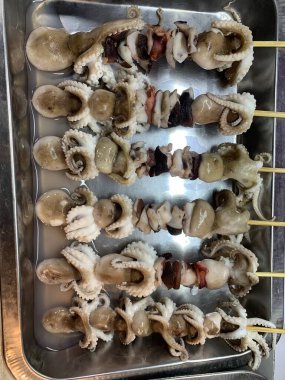 Açık hava yiyecek pazarında servis edilen bambu çubuğuyla ızgara yapılmış lezzetli kalamar ve ahtapot. egzotik Asya yemekleri. 