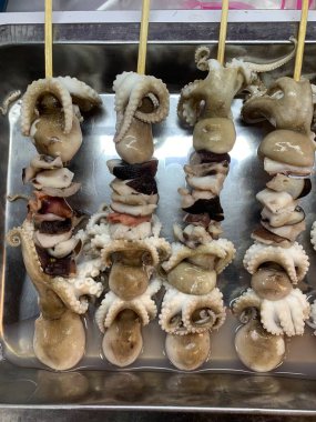 Açık hava yiyecek pazarında servis edilen bambu çubuğuyla ızgara yapılmış lezzetli kalamar ve ahtapot. egzotik Asya yemekleri. 